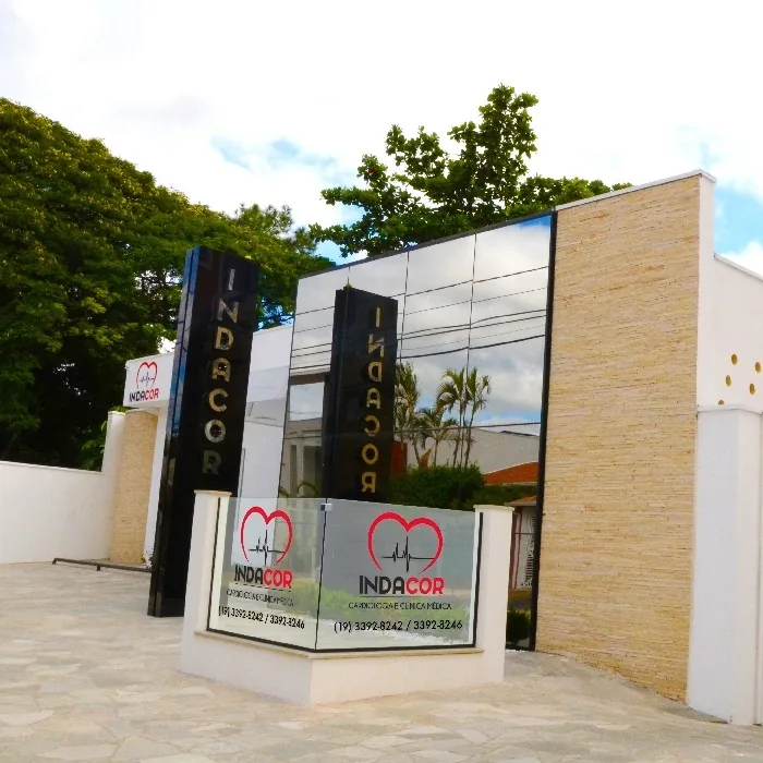 Fachada moderna da clínica Indacor em Indaiatuba, com painéis de vidro reflexivo, parede de pedra clara e letreiro com logotipo de cardiologia.
